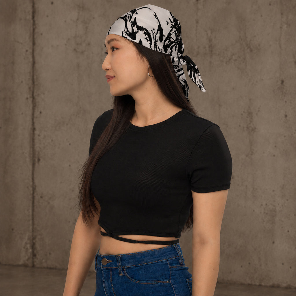 Woman wearing Ink-Riot Bandana as a headband, black and white all-over print, styled with a black crop top and jeans against a concrete wall